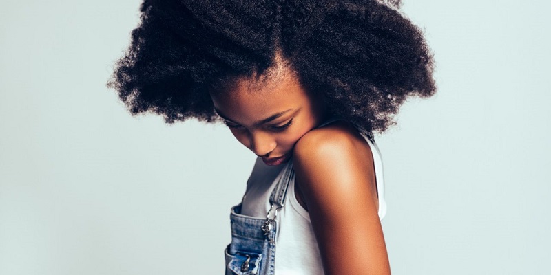 Shy young African girl standing sideways against a gray backgrou