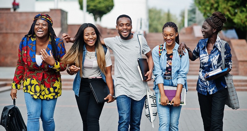 Group of five african college students spending time together on campus at university yard. Black afro friends studying. Education theme.